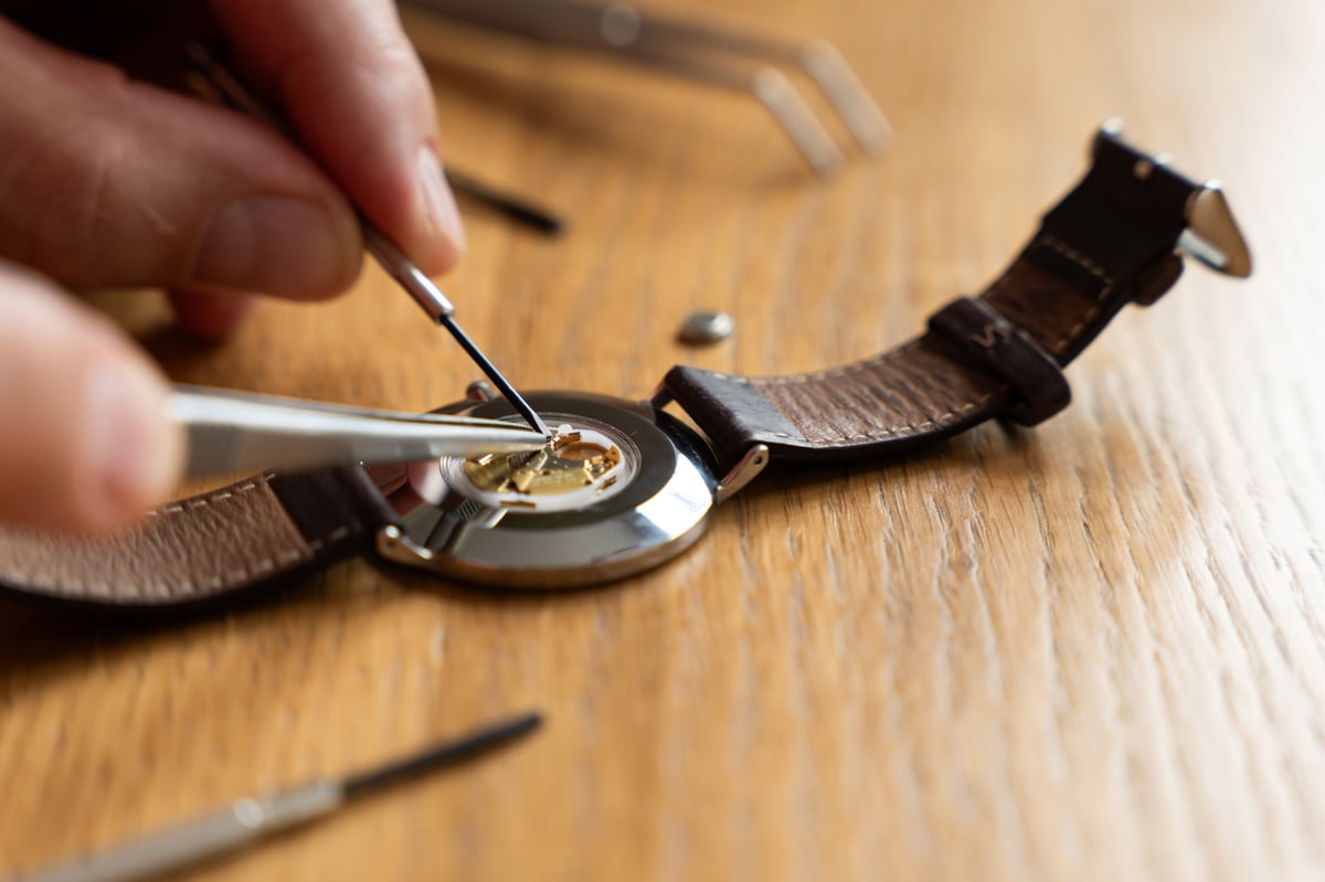 Horlogemaker werkt met een pincet aan een mechanisch uurwerk op een houten werkbank