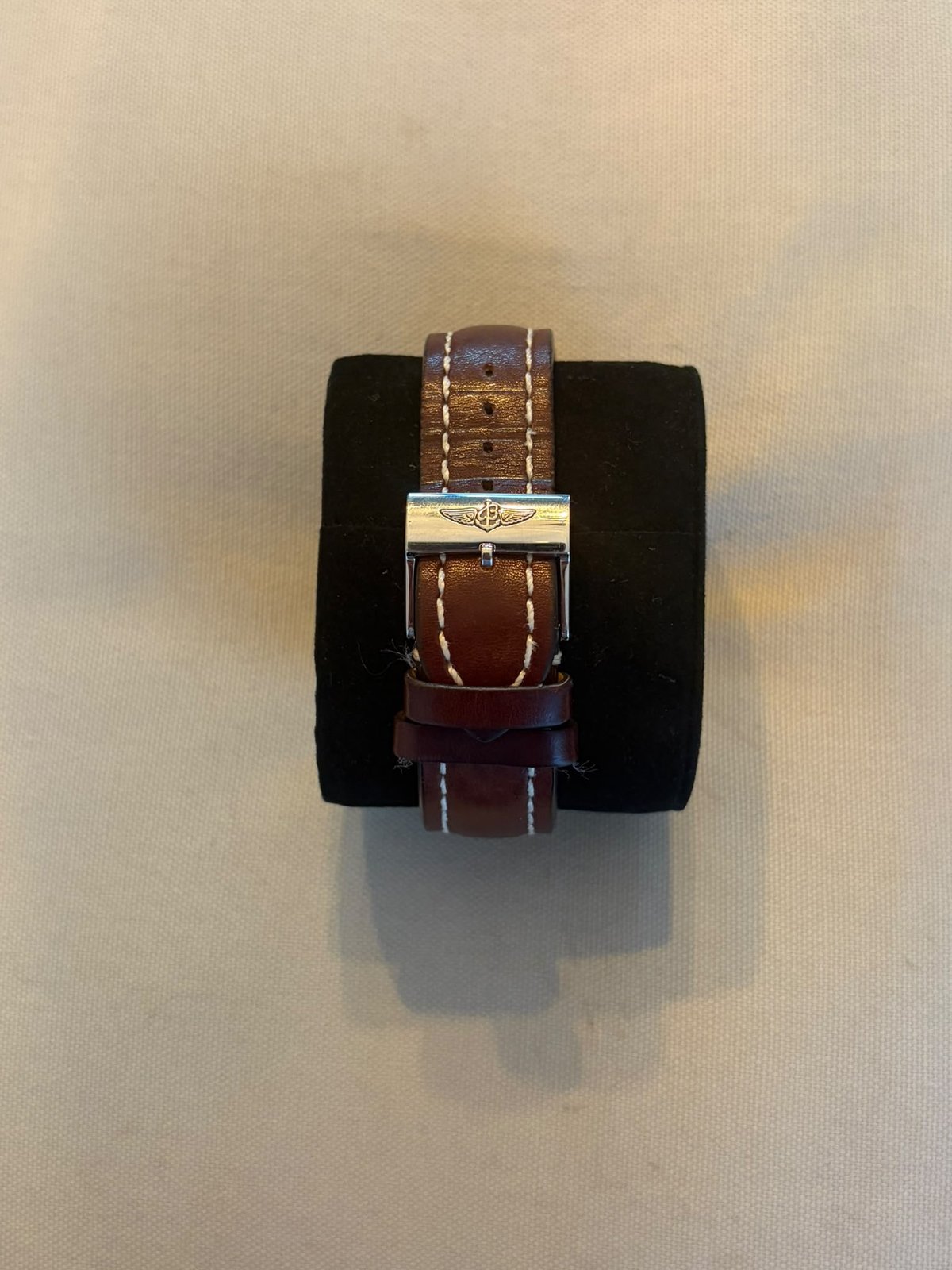 Breitling leather strap with stainless steel Breitling pin buckle on a black watch stand against a beige background